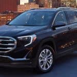 A black 2020 GMC Terrain is parked on a roof top parking lot with city lights in the background.