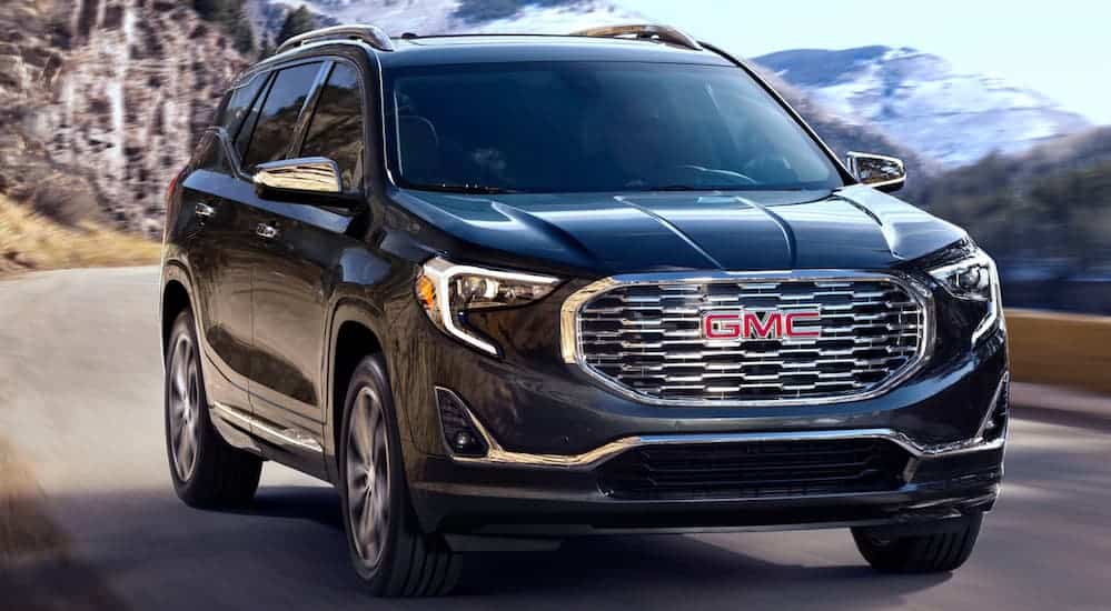 A black 2020 GMC Terrain is driving on a hill side road with mountains in the background. 