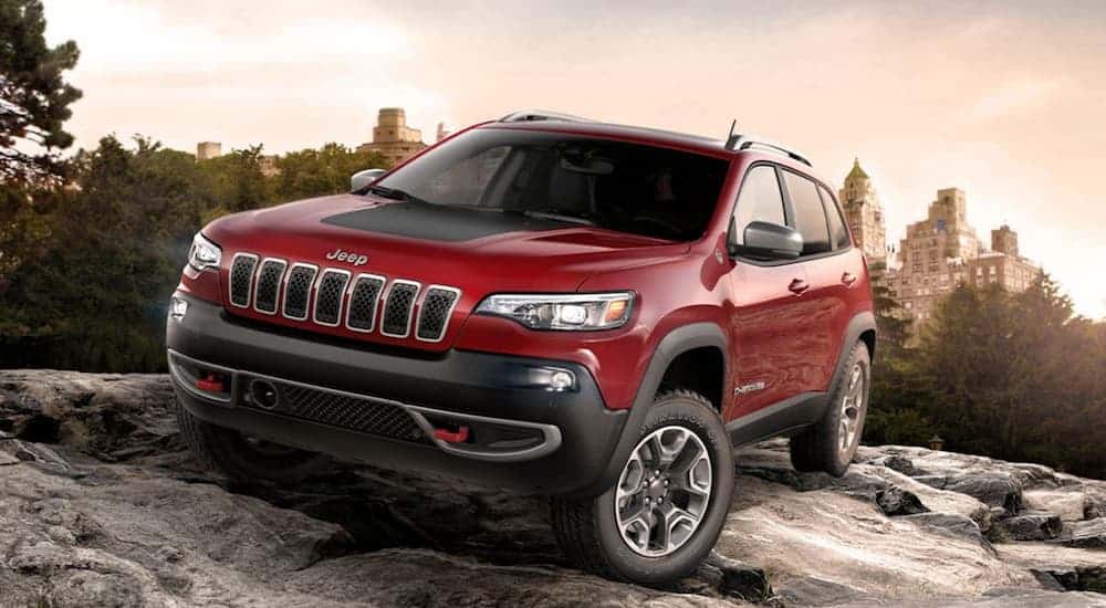 A red 2020 Jeep Cherokee Trailhawk is driving on a large rock through the woods.