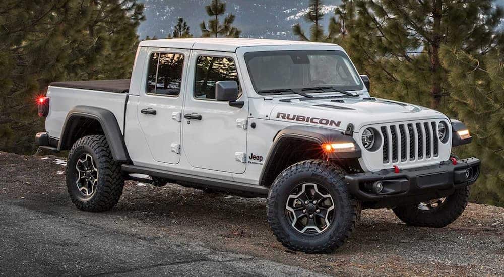 A white 2020 Jeep Gladiator Rubicon is parked on a dirt trail that's overlooking snow covered mountains.