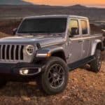 A 2020 silver Jeep Gladiator is parked on a dirt hill overlooking a valley.
