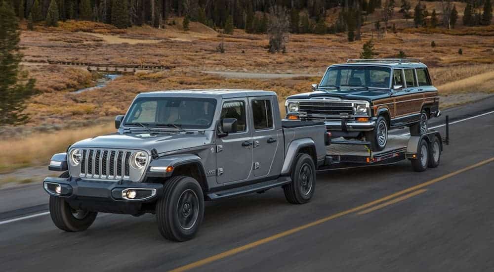 A grey 2020 Jeep Gladiator is towing a Grand Wagoneer on a grasslined highway. 