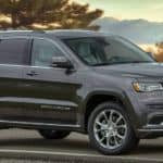 A grey 2020 Jeep Grand Cherokee is parked on a road that's overlooking a lake at dusk.