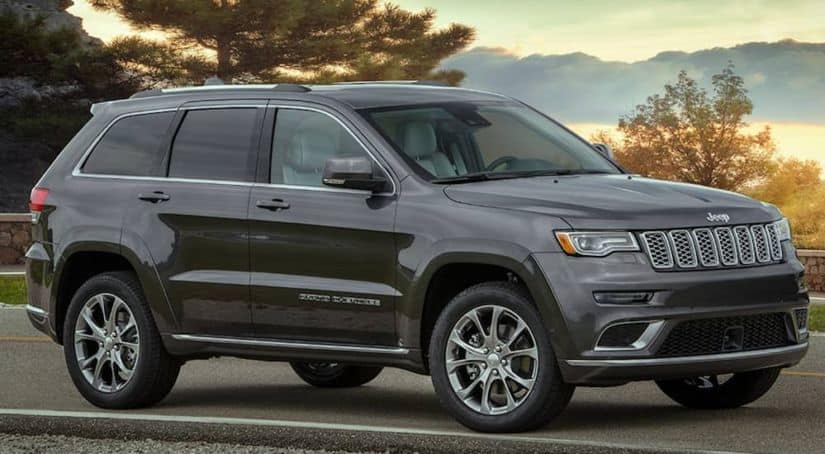 A grey 2020 Jeep Grand Cherokee is parked on a road that's overlooking a lake at dusk.