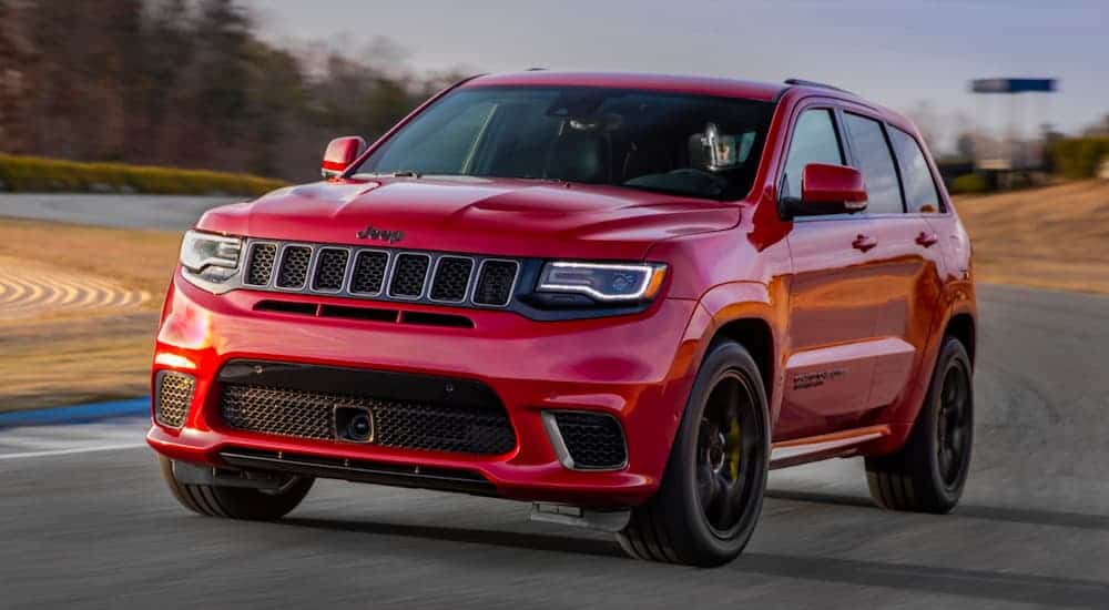 A red 2020 Jeep Grand Cherokee Trackhawk is driving around a corner on a racetrack at dusk.