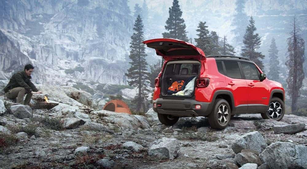A man is starting a fire next to his red 2020 Jeep Renegade, which wins when comparing the 2020 Jeep Renegade vs 2020 Ford EcoSport, in the middle of the woods. 