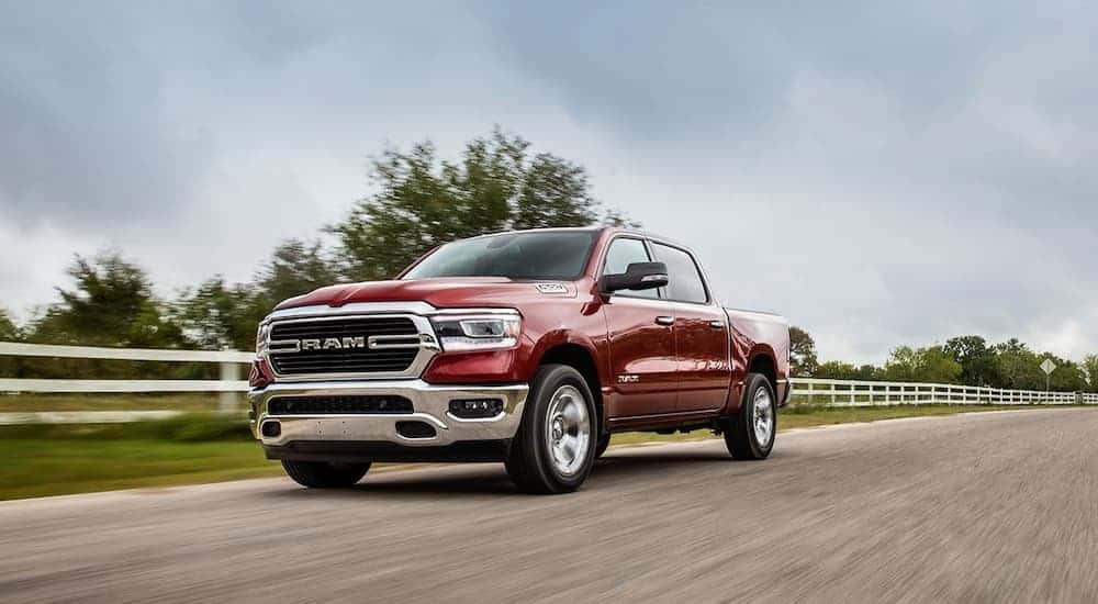 A red 2020 Ram 1500, which wins when comparing the 2020 Ram 1500 vs 2020 Chevy Silverado 1500, is driving past a farm.