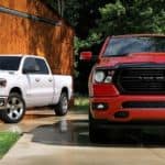A white 2020 Ram 1500 is parked next to a red one in front of a barn.