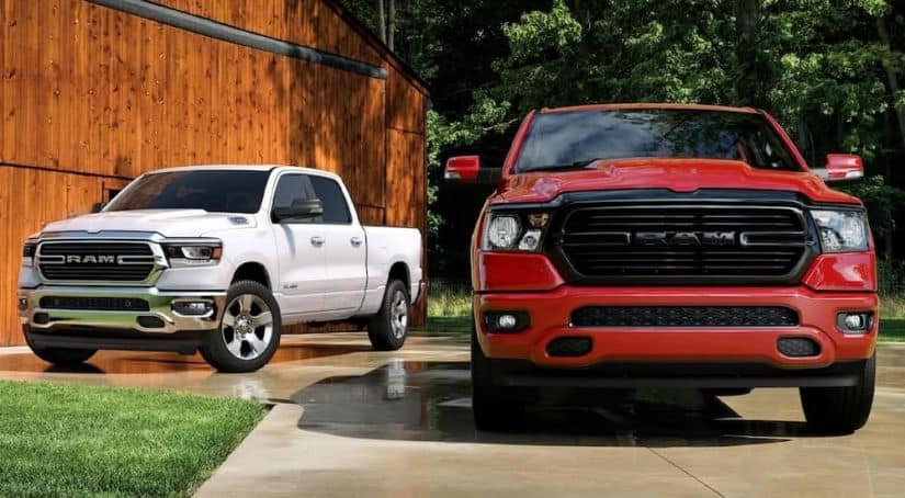 A white 2020 Ram 1500 is parked next to a red one in front of a barn.