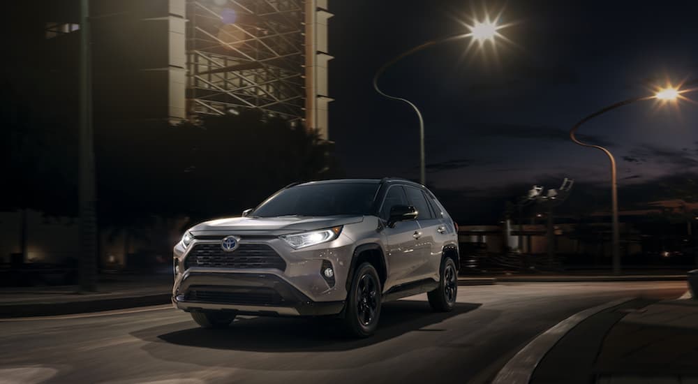 A gray 2020 Toyota RAV4 is driving city street at night in front of curvy street lights