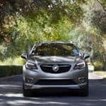 A grey 2020 Buick Envision is driving on a tree-lined street.