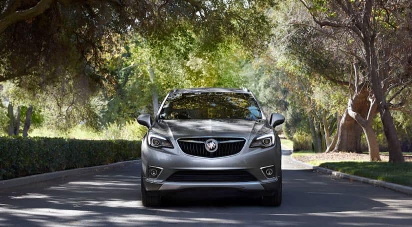 A grey 2020 Buick Envision is driving on a tree-lined street.