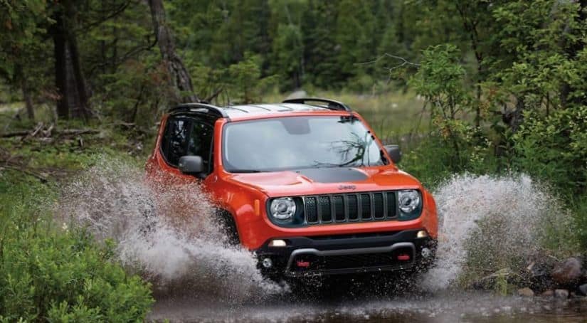 An orange 2020 Jeep Renegade is driving through a large puddle with water spraying up.