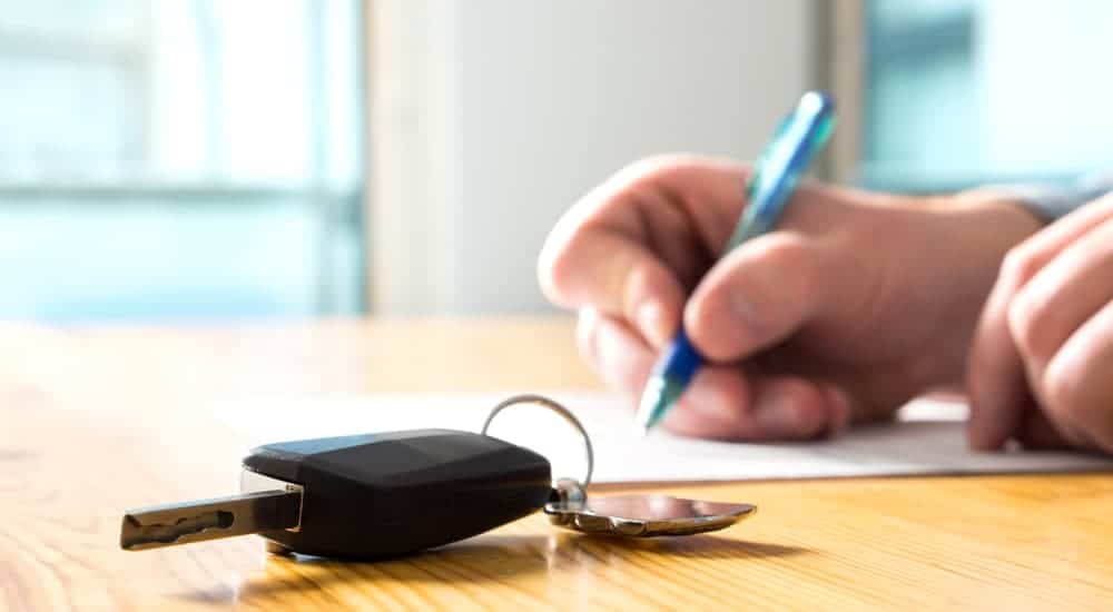A customer is signing warranty papers, which is something that you should look for when looking at Factory Certified Pre-Owned vs Dealer Certified Pre Owned, at a used car dealership.