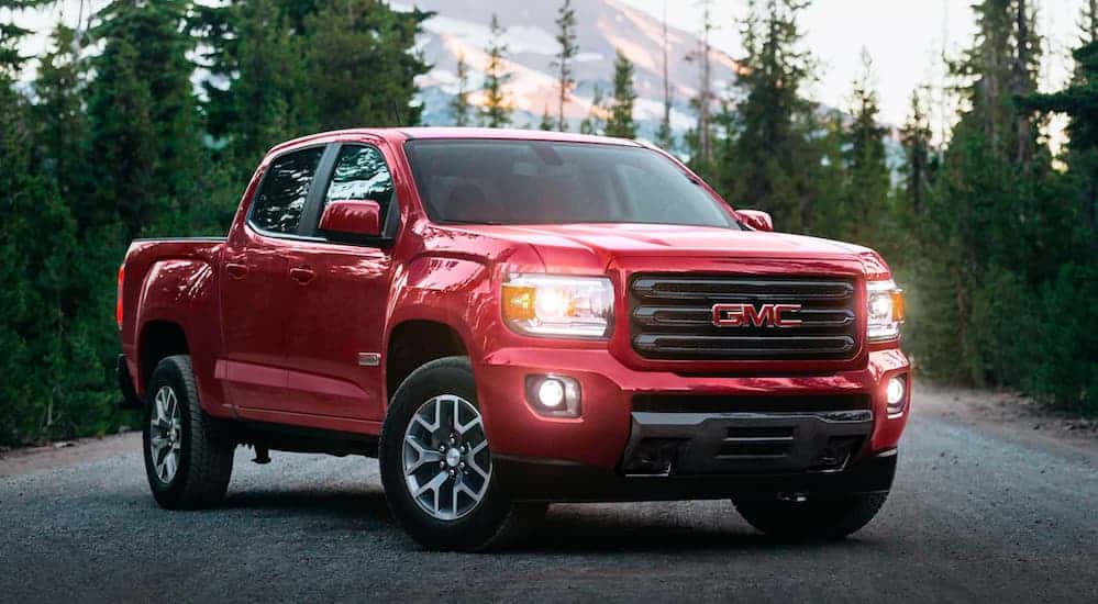 A red 2020 GMC Canyon, which is a popular option at a GMC dealer near me, is parked on a pine tree lined road.