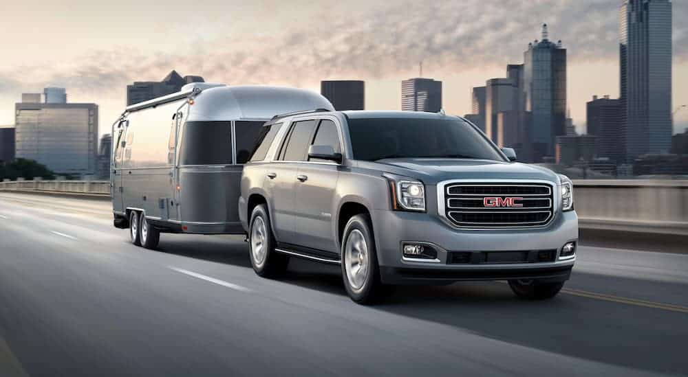 A silver 2020 GMC Yukon is towing an Airstream on a highway with a city sky line in the distance. 
