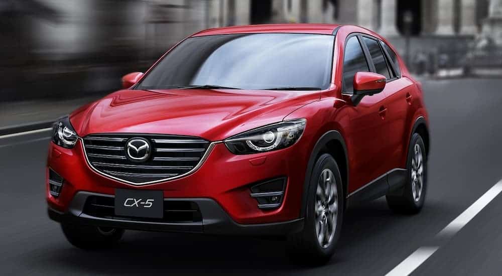 A red 2015 Mazda CX-5 is driving on a city street.