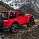 A red 2018 Jeep Wrangler is parked off-road with a mountain view.