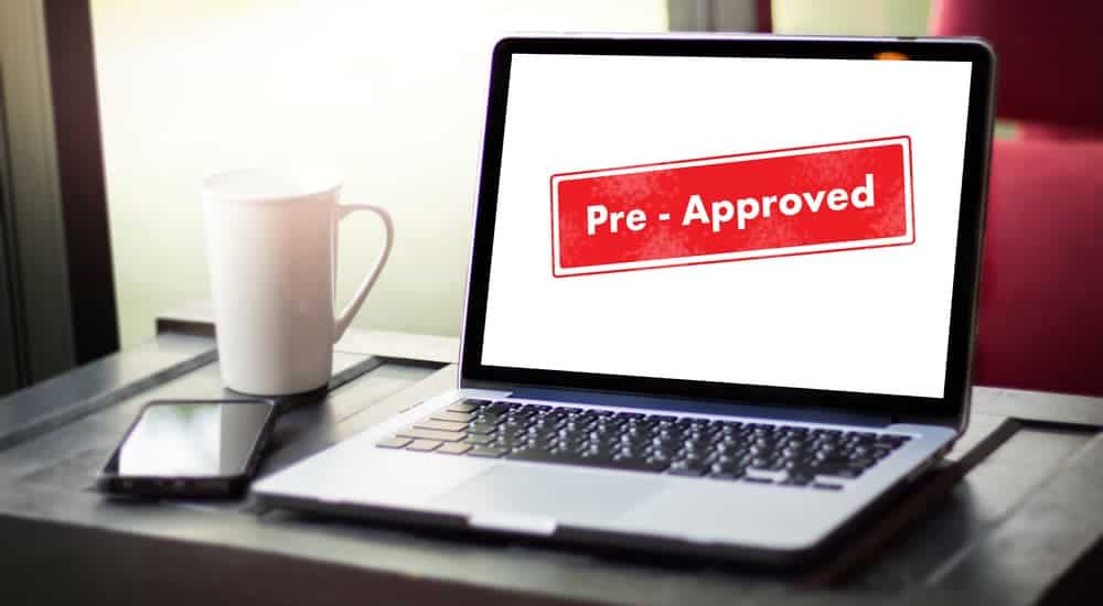 A red pre-approved stamp, which a task you want to do while looking for a bad credit car loan, is shown on a laptop screen.