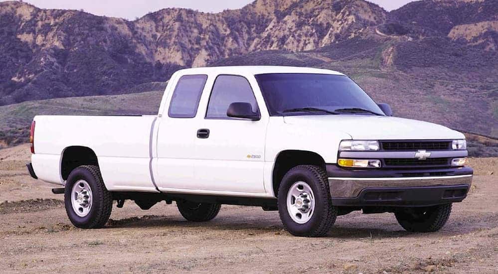 A white 1999 used Chevy Silverado 1500 is parked on a dirt trail with mountains in the distance. 