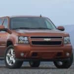 An orange 2011 Chevrolet Avalanche is parked on a gravel parking lot with mountains in the distance.