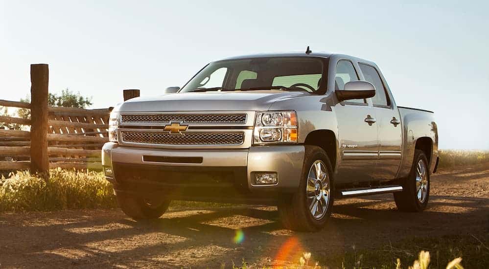 A silver 2013 Chevy Silverado is parked at a farm while the sun sets in the distance. 