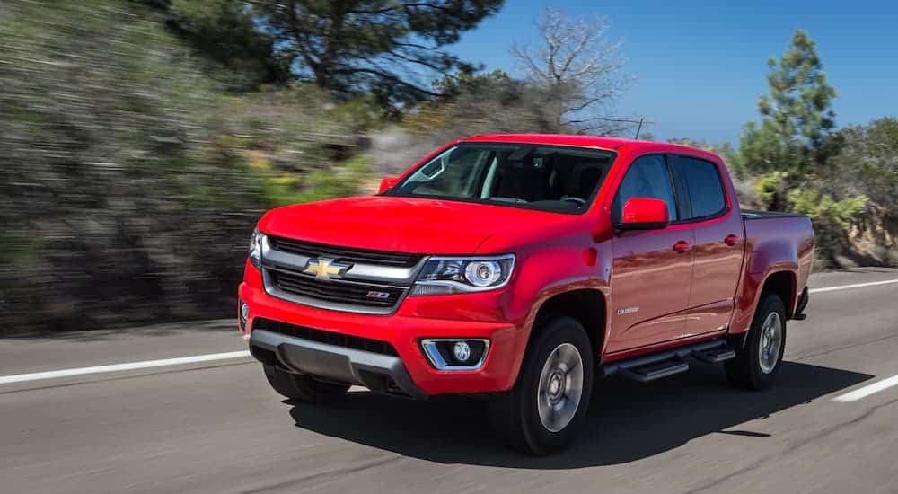 A red 2015 Chevrolet Colorado, which is a popular option among used Chevy trucks, is driving on a tree lined road. 