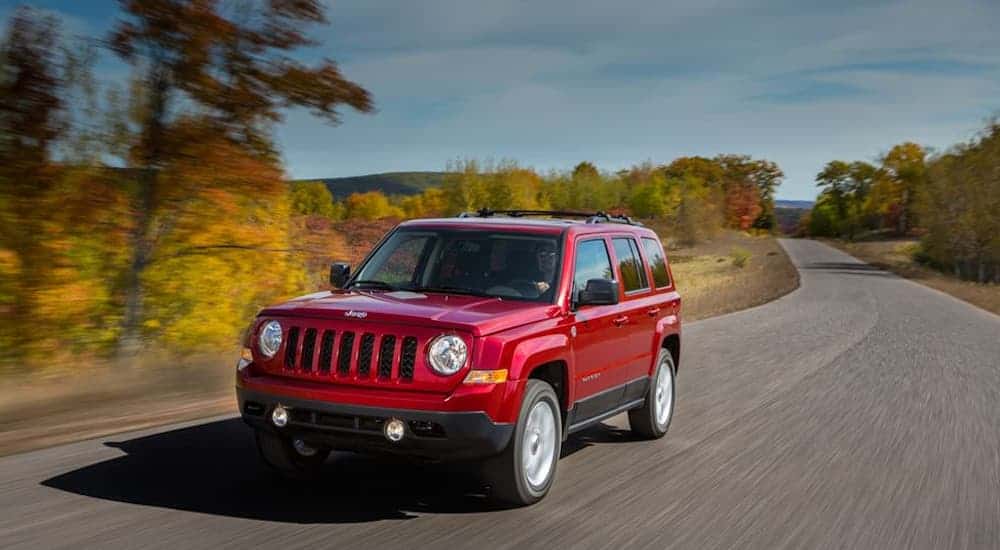A red 2016 Jeep Patriot, which is a popular option among used cars for sale, is driving on a rural road in fall