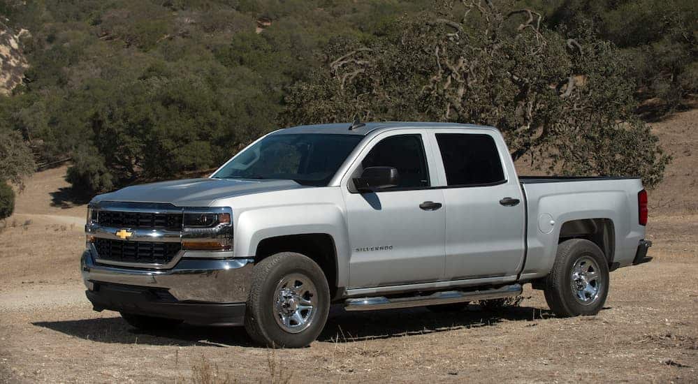A silver 2018 Chevy Silverado, which is a common model among the used Chevy Silverado 1500's, is parked on a dirt road. 