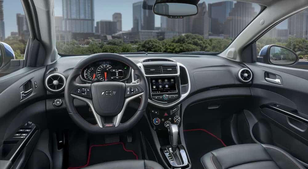 The front black and grey interior of the 2020 Chevy Sonic is shown with an infotainment system. 