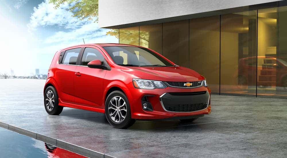 A red 2020 Chevy Sonic hatchback is parked in front of large glass windows in a house. 
