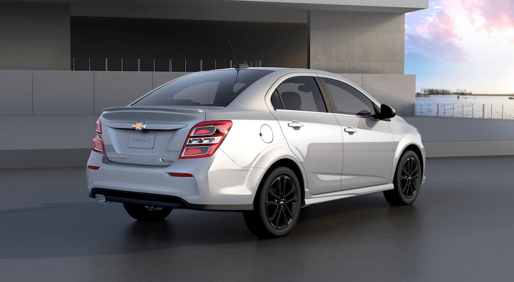 A silver 2020 Chevy Sonic sedan is parked in front a cement building. 