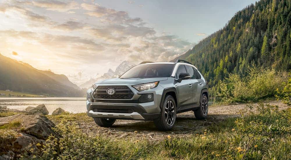 A sage green 2020 Toyota RAV4 is parked next to a lake with mountains behind it.