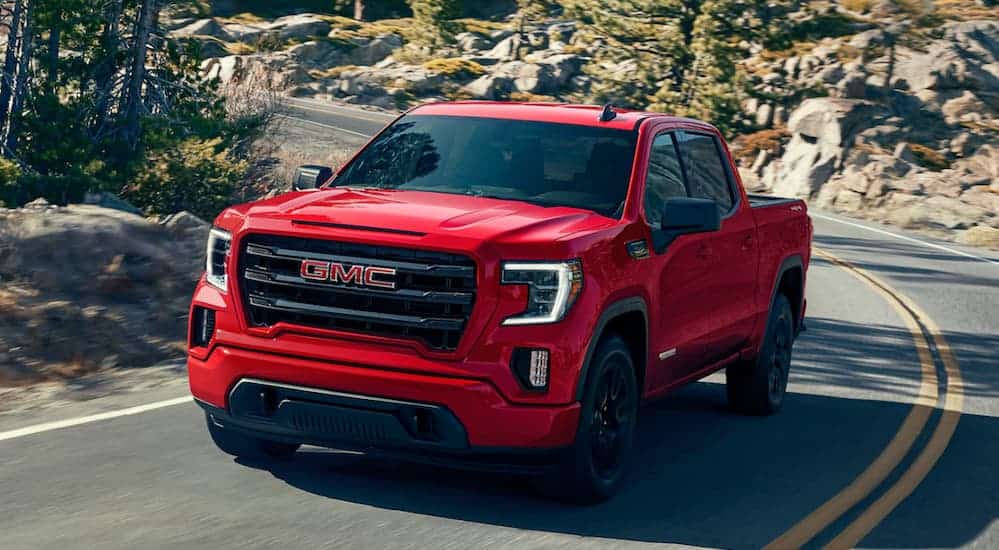 A red 2020 GMC Sierra 1500, which wins when comparing the 2020 GMC Sierra 1500 vs 2020 Ram 1500, is driving on a treelined road. 