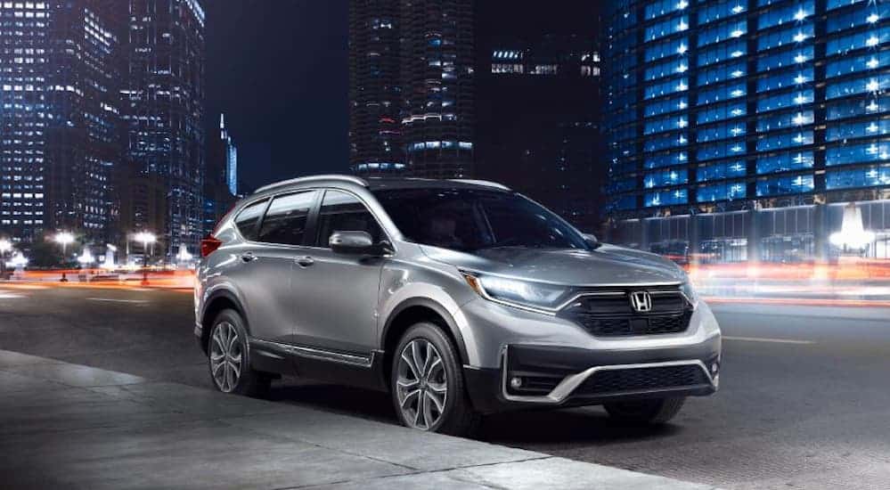 A grey 2020 Honda CR-V is parked on the side of a busy city street at night. 