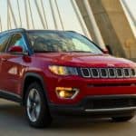 A red 2020 Jeep Compass is driving on a bridge at dusk.