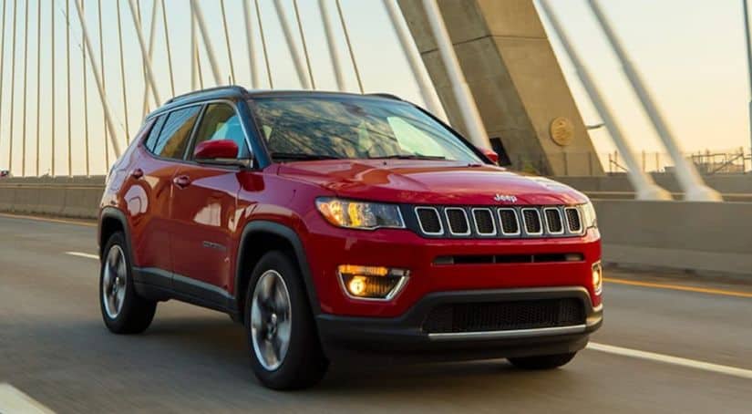 A red 2020 Jeep Compass is driving on a bridge at dusk.
