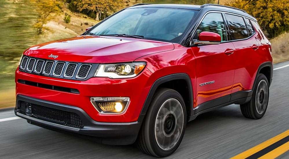 A red 2020 Jeep Compass is driving on a treelined road.