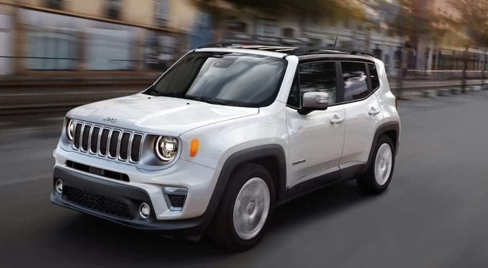 A white 2020 Jeep Renegade is driving on a city street passed blurry buildings. 