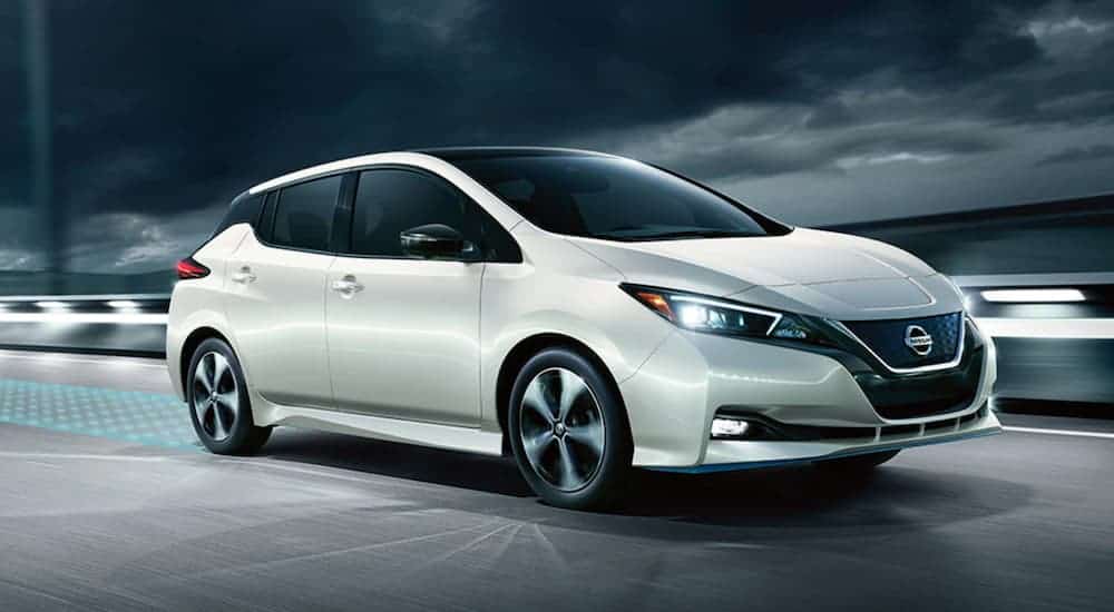 A white 2020 Nissan Leaf is driving on a bridge at night.