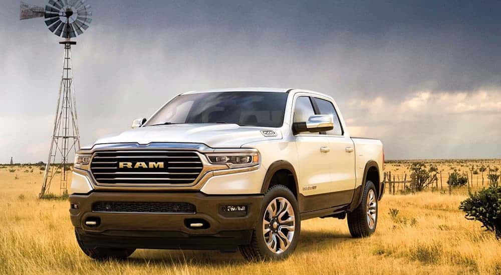 A white 2020 Ram 1500 is parked in a grassy field with a windmill behind it. 
