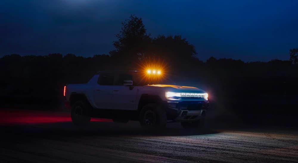 A white 2022 GMC Hummer EV is shown in the dark with its headlights and light bar illuminated.