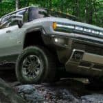 A grey 2022 GMC Hummer EV is shown from the front while driving over a rocky path in the woods..