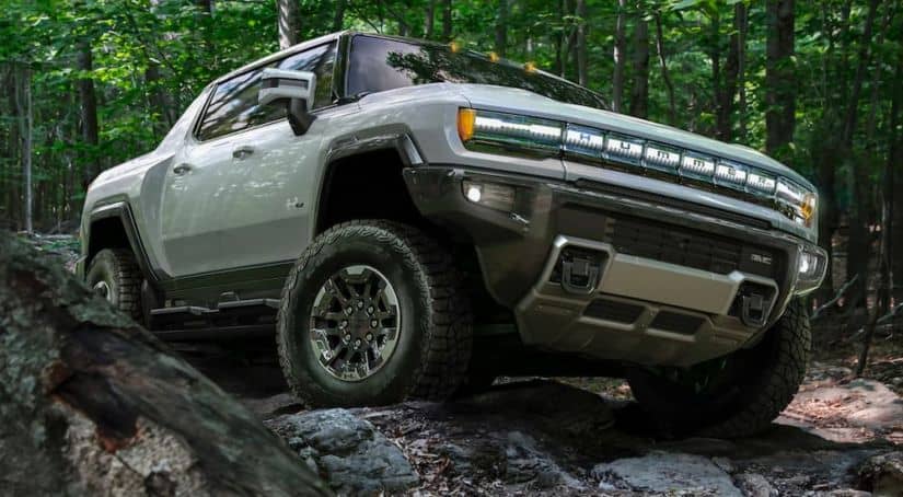 A grey 2022 GMC Hummer EV is shown from the front while driving over a rocky path in the woods..