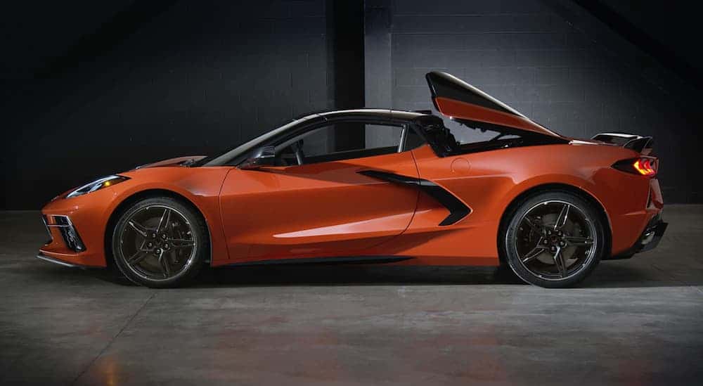 A side view of an orange 2020 Chevy Corvette, a popular performance car at a local Chevy dealership, has the two-piece hardtop lifting.