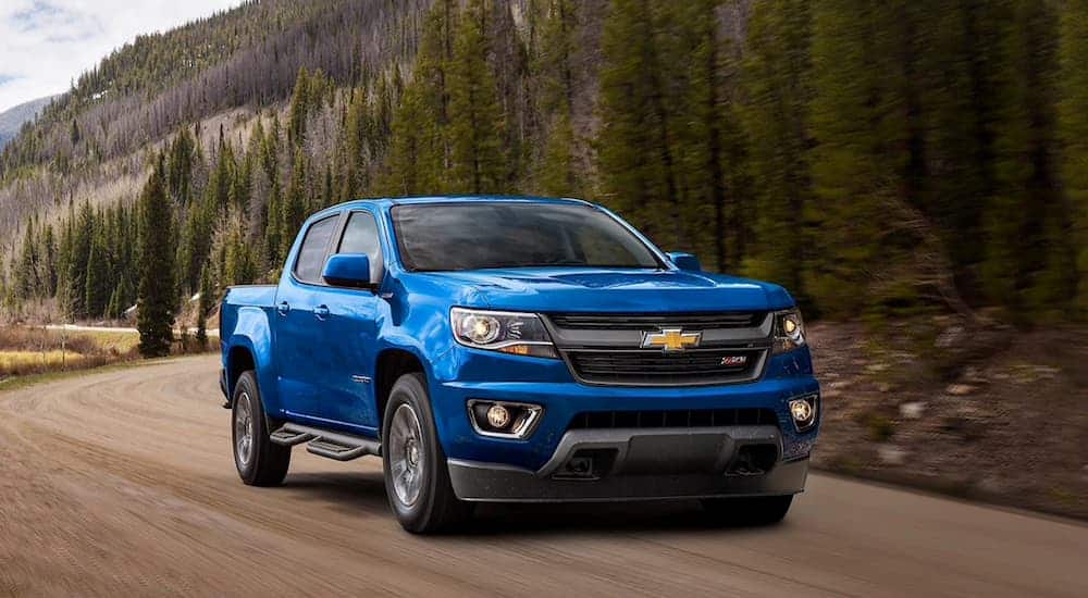 A blue 2020 Chevy Colorado, popular among Chevy trucks, is driving on a dirt road.