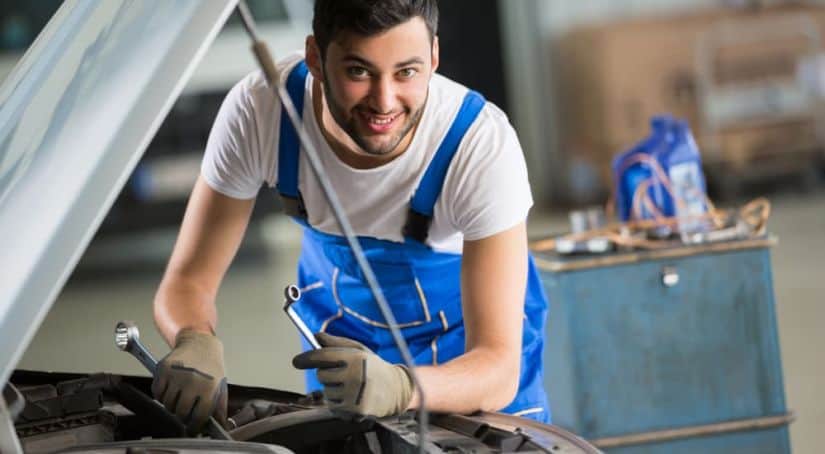 A smiling mechanic is working on a customer's car at a dealership.