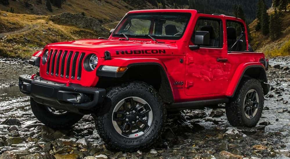 A red topless 2020 Jeep Wrangler 2-door is driving on small rocks in the middle of a valley. 