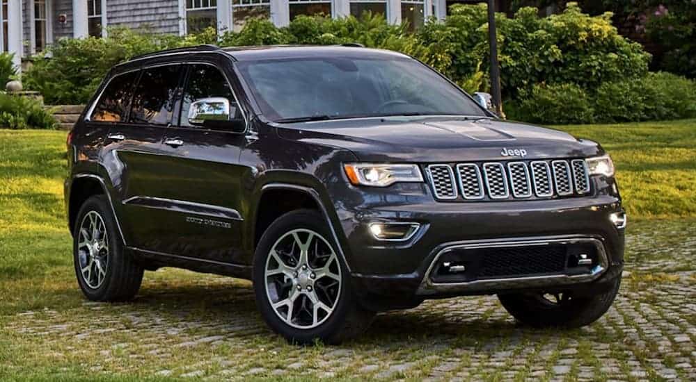 A black 2020 Jeep Grand Cherokee is parked on grass in front of a large home.