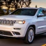A white 2020 Jeep Grand Cherokee for sale is driving on a treelined road.